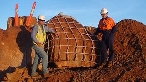 Michael Smith standing beside a large rock wrapped in containment mesh, on red ground.